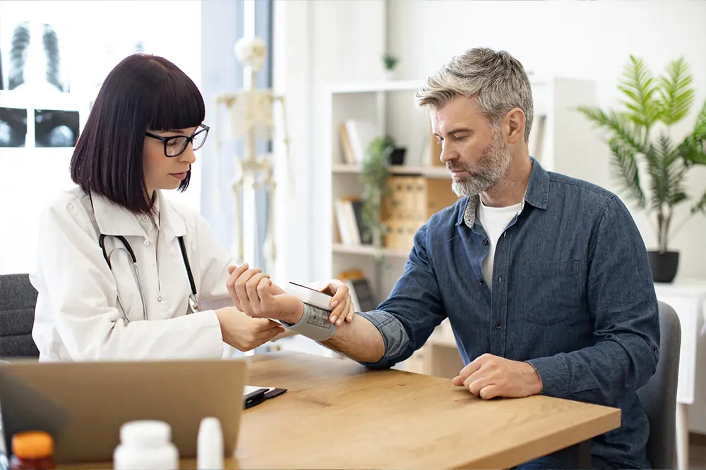 A female doctor checks a male patient's blood pressure with a cuff in a modern clinic setting.